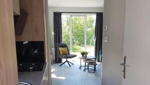 A modern kitchen with a built-in oven, a dining area with a table and chairs, and a trash bin. - Chalet 34 (4 persons) (Petten)
