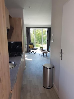 A modern kitchen with a built-in oven, a dining area with a table and chairs, and a trash bin. - Chalet 34 (4 persons) (Petten)