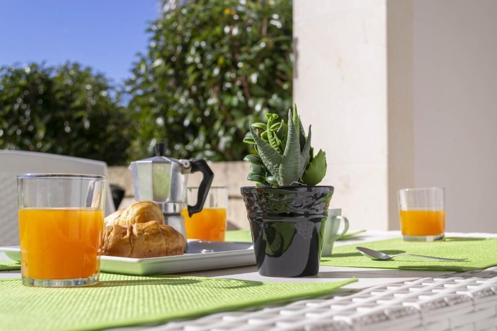 A breakfast setup with a croissant, two glasses of orange juice, a coffee pot, and a potted plant on a table.