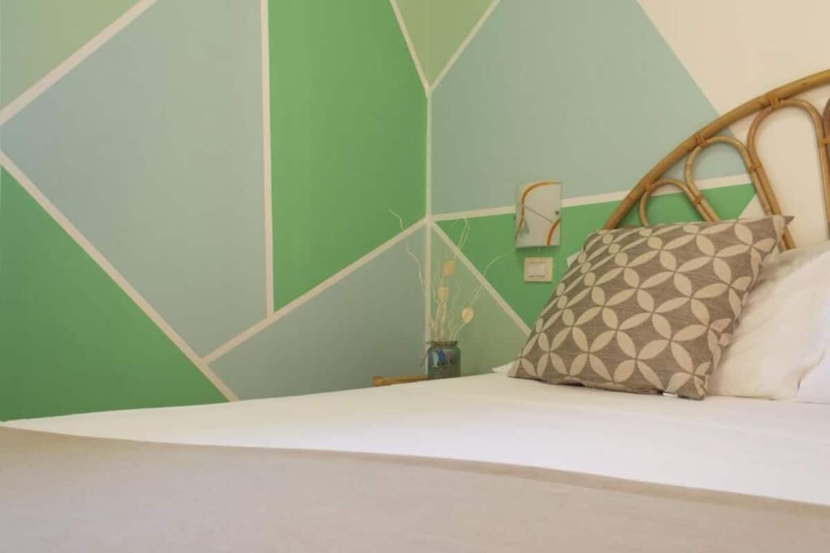 A bed with a white mattress, a patterned pillow, and a wicker headboard.