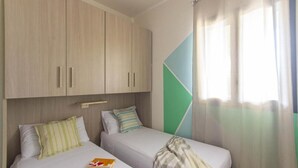 Un dormitorio con dos camas, un armario, un diseño geométrico en la pared y una ventana con cortinas.