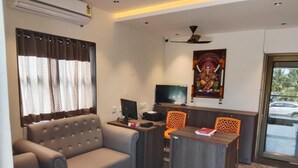 A living room with a sofa, a desk, a television, and a ceiling fan. - Sam's Court Elite Stay (Manachanallur)