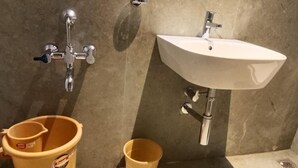 A bathroom with a white sink, a handheld showerhead, and two buckets. - Sam's Court Elite Stay (Manachanallur)