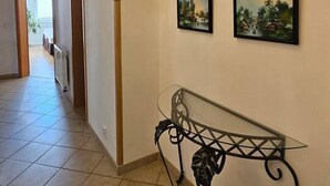 Un pasillo con un candelabro, una mesa con cubierta de vidrio y varias pinturas de paisajes enmarcadas en la pared.