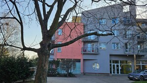Un edificio residencial de varios pisos con un patio central, un árbol en primer plano y un coche estacionado.