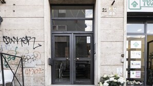 A building with a double door entrance, a concrete wall with graffiti, and a small flower arrangement outside. - Baronio@home - One Bedroom Apartment, Sleeps 4 (Rome)