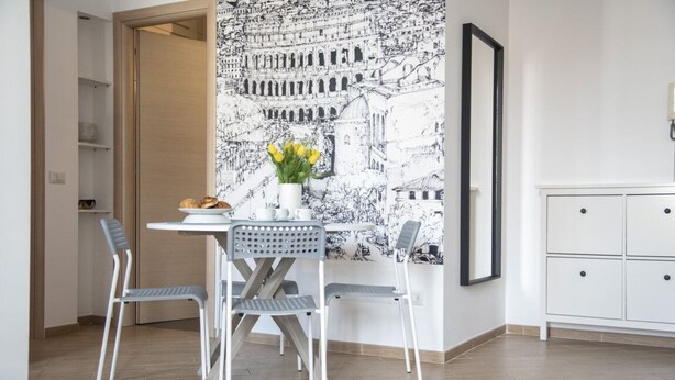A dining area with a table, chairs, a vase with flowers, and a wall with a black and white cityscape mural. - Baronio@home - One Bedroom Apartment, Sleeps 4 (Rome)