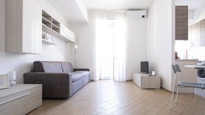 A modern living room with a sofa, a TV, a side table, a chair, and built-in shelving. - Baronio@home - One Bedroom Apartment, Sleeps 4 (Rome)