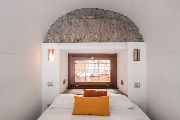 A bedroom with a bed, a window with a view, and a stone arch above the door. - Mini-Loft Piazza di Spagna (Rome)