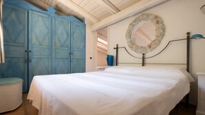 Een slaapkamer met een bed, een blauwe garderobe, een ronde spiegel en een witte nachtkastje.