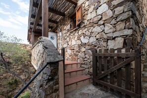 Ein Steinhaus mit einer Holztreppe, die zu einer Tür führt, einem Holztor und einer Steinmauer.