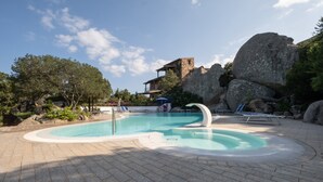 Een zwembad met een jacuzzi, ligbedden en een stenen gebouw op de achtergrond.