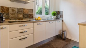 A kitchen with white cabinets, a stainless steel range hood, a window with a view of greenery, and a tiled backsplash. - Santonofrio Colors - Three Bedroom Apartment, Sleeps 8 (Rome)