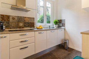 A kitchen with white cabinets, a stainless steel range hood, a window with a view of greenery, and a tiled backsplash. - Santonofrio Colors - Three Bedroom Apartment, Sleeps 8 (Rome)