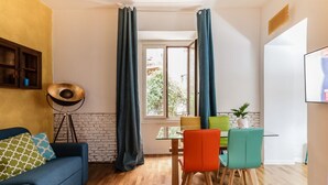 A modern living space with a sofa, dining table, chairs, a lamp, and a window with curtains. - Santonofrio Colors - Three Bedroom Apartment, Sleeps 8 (Rome)