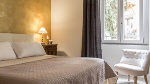 A bedroom with a bed, a nightstand, a lamp, a chair, and a window with curtains. - Santonofrio Gold - Two Bedroom Apartment, Sleeps 5 (Rome)