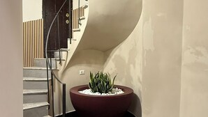 A curved staircase with a dark floor, a red planter with white pebbles, and a door in the background. - Santonofrio Gold - Two Bedroom Apartment, Sleeps 5 (Rome)