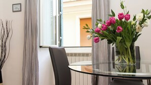 A dining area with a glass table, black chairs, a vase of flowers, and a window with curtains. - Santonofrio Silver - One Bedroom Apartment, Sleeps 4 (Rome)