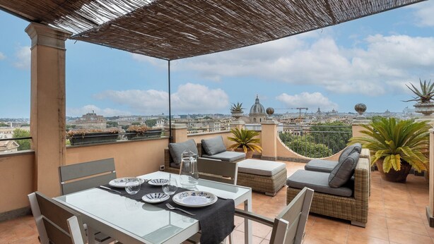 Una terraza en la azotea con mesa lista para comer, asientos acolchados y plantas en macetas.