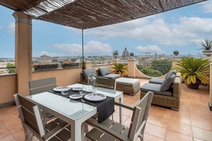 A rooftop terrace with a table set for dining, cushioned seating, and potted plants. - Santonofrio SKY Terrace Penthouse (Rome)