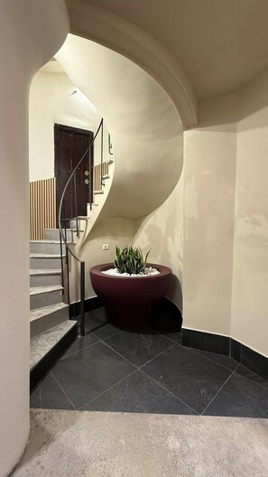 A curved staircase with a dark floor, a red planter with white pebbles, and a door in the background. - Santonofrio White - One Bedroom Apartment, Sleeps 4 (Rome)
