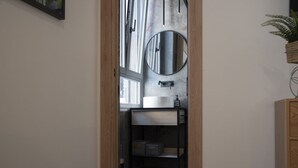 A narrow hallway leading to a bathroom with a large mirror, a window, and a wooden cabinet. - Vatican Boutique Apartment St. Peter Dome View (Rome)