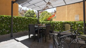An outdoor patio with a table and chairs, a white umbrella, and a hedge. - Vatican Boutique Apartment with Large Terrace (Rome)
