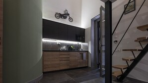 A modern kitchen with dark cabinets, a motorcycle decoration, and a staircase with wooden steps. - Vatican Boutique Apartment with Large Terrace (Rome)