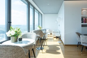 Een moderne zithoek met rieten stoelen, een ronde tafel en een boekenkast.