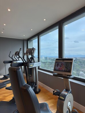 Una palestra con tapis roulant ed ellittica, uno schermo televisivo e un'ampia finestra con vista sulla città.