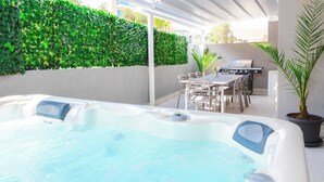 Ein Whirlpool mit Tisch und Stühlen, umgeben von einer Hecke und einem Grill.