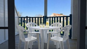 Eine überdachte Terrasse im Freien mit einem Tisch und vier weißen Stühlen, einer Karaffe mit Zitronenscheibe und einem strahlend blauen Himmel.