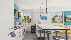 Eine moderne Küche mit integriertem Waschmaschine, einer Bar mit Barhocker und großen Fenstern mit Blick ins Freie.