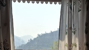 Une pièce offrant une vue sur un paysage vallonné, visible à travers une fenêtre ornée de rideaux légers et transparents.