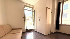 Una habitación con sofá, puerta corredera y ventana con vistas a edificios.