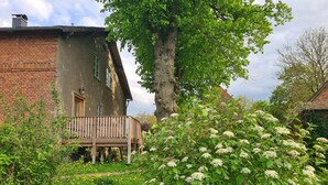 Una casa rústica amb una terrassa de fusta, una paret de maó i un arbre gran al pati.