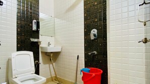 A bathroom with a toilet, sink, shower, and a red bucket. - Hotel RAJ (Haridwar)