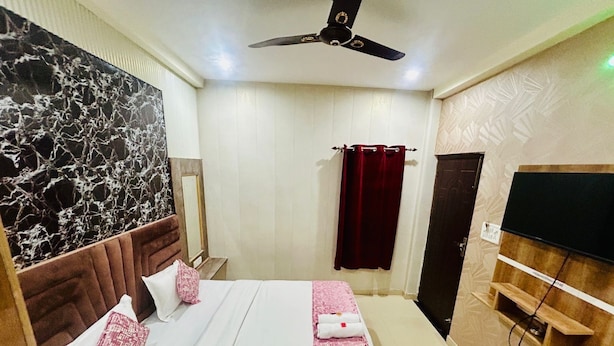 A hotel room with a bed, a ceiling fan, a TV, a wooden chair, and a mirror. - Hotel RAJ (Haridwar)