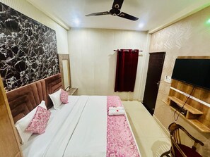 A hotel room with a bed, a ceiling fan, a TV, a wooden chair, and a mirror. - Hotel RAJ (Haridwar)