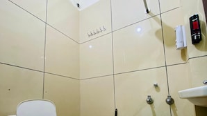 A small bathroom with a toilet, a mop, a blue bucket, and a showerhead. - Hotel RAJ (Haridwar)