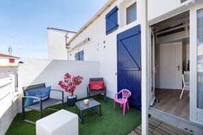 A small outdoor seating area with a bench, chairs, and a table, surrounded by a white wall and blue shutters. - La Pause Iodée – Close to Beaches and Town Center (La Tranche-sur-Mer)