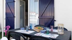 An outdoor dining area with a table set for two, a wicker basket with fruits, and a wicker lantern. - La Pause Iodée – Close to Beaches and Town Center (La Tranche-sur-Mer)