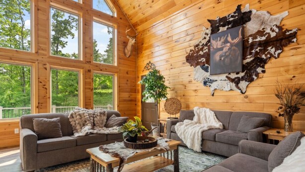 A log cabin interior with two sofas, a coffee table, and a mounted deer head. - Fernwood Lodge - 15 Min To Raystown Lake (Huntingdon)