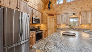 A kitchen with wooden cabinets, a stainless steel refrigerator, a granite countertop, and a microwave. - Fernwood Lodge - 15 Min To Raystown Lake (Huntingdon)