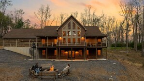 A large, multi-story lodge with a prominent central tower, a covered front porch, and a fire pit area. - Fernwood Lodge - 15 Min To Raystown Lake (Huntingdon)