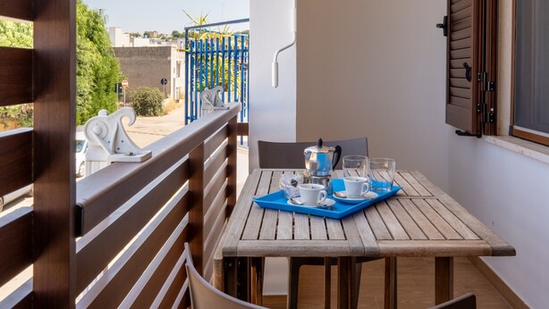 A balcony with a wooden table set for two, a coffee pot, and two cups.