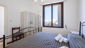 A bedroom with a bed, a chair, a wardrobe, a window, and a ceiling light fixture.