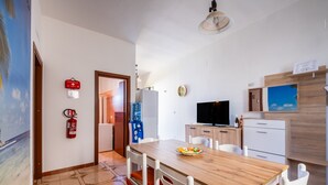 A modern kitchen with white cabinets, a wooden dining table, and a television.