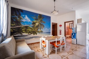 A room with a beach mural, a dining table with chairs, a sofa, a water dispenser, and a refrigerator. - Holiday Home 'Vacanza Alle 4 Colonne - 1' with Balcony, Wi-Fi and Air Conditioning (Santa Maria al Bagno)