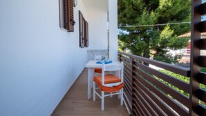 A balcony with a table and chairs, a railing, and a view of trees and buildings.
